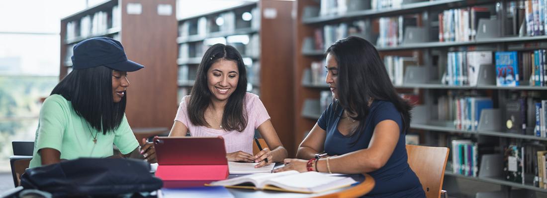 three female students sitting at a table in a college library